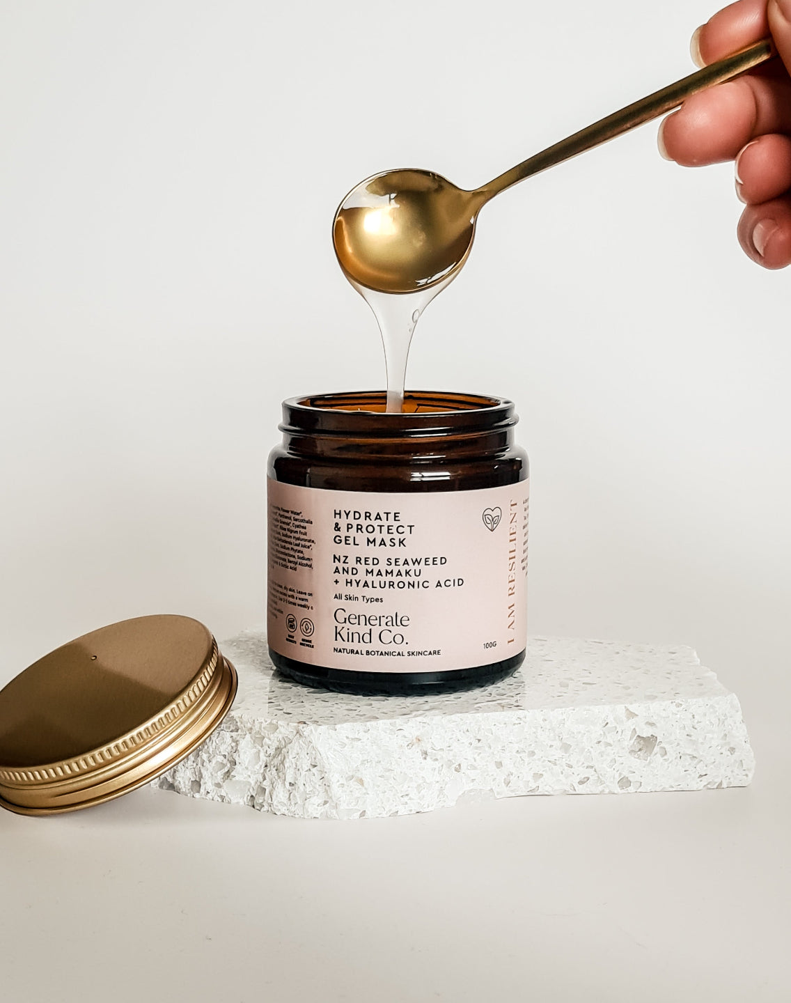 Hand holding a spoon pouring gel into a jar labeled 'Generate Hand Co.' on a white background