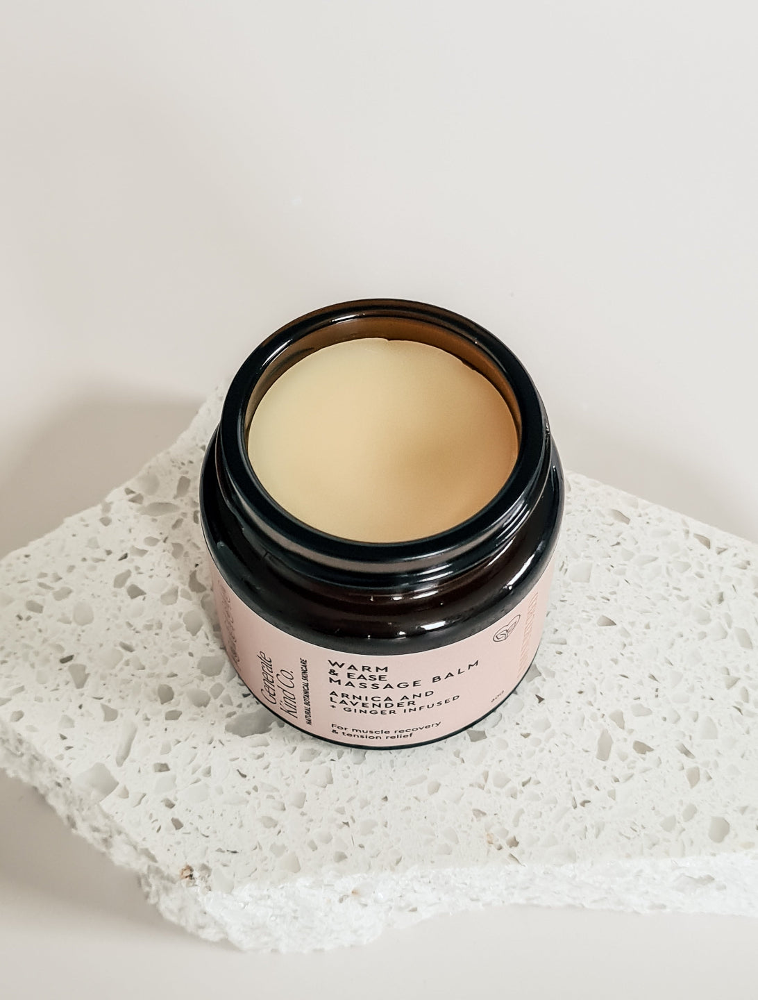 Jar of massage balm on a textured stone surface with a light background