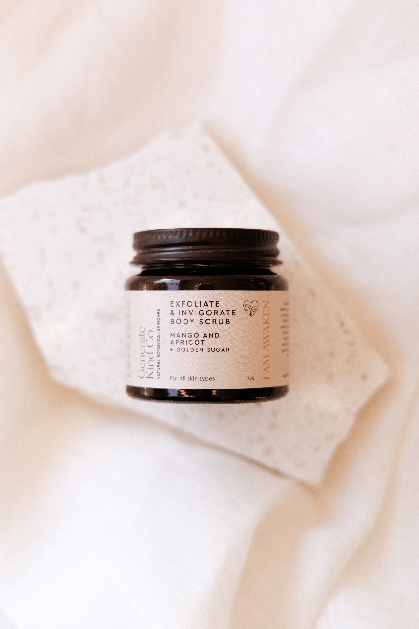 Jar of Generate Kind CO. Sugar body scrub on a soft fabric background