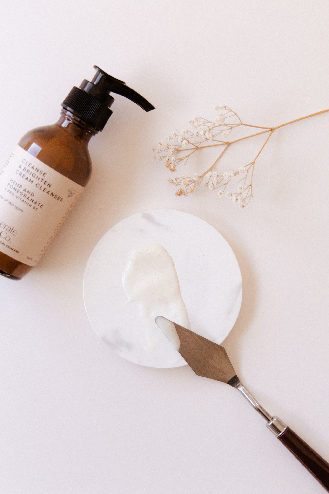 Cream Cleanser showing texture on spatula and dried flowers on a light background