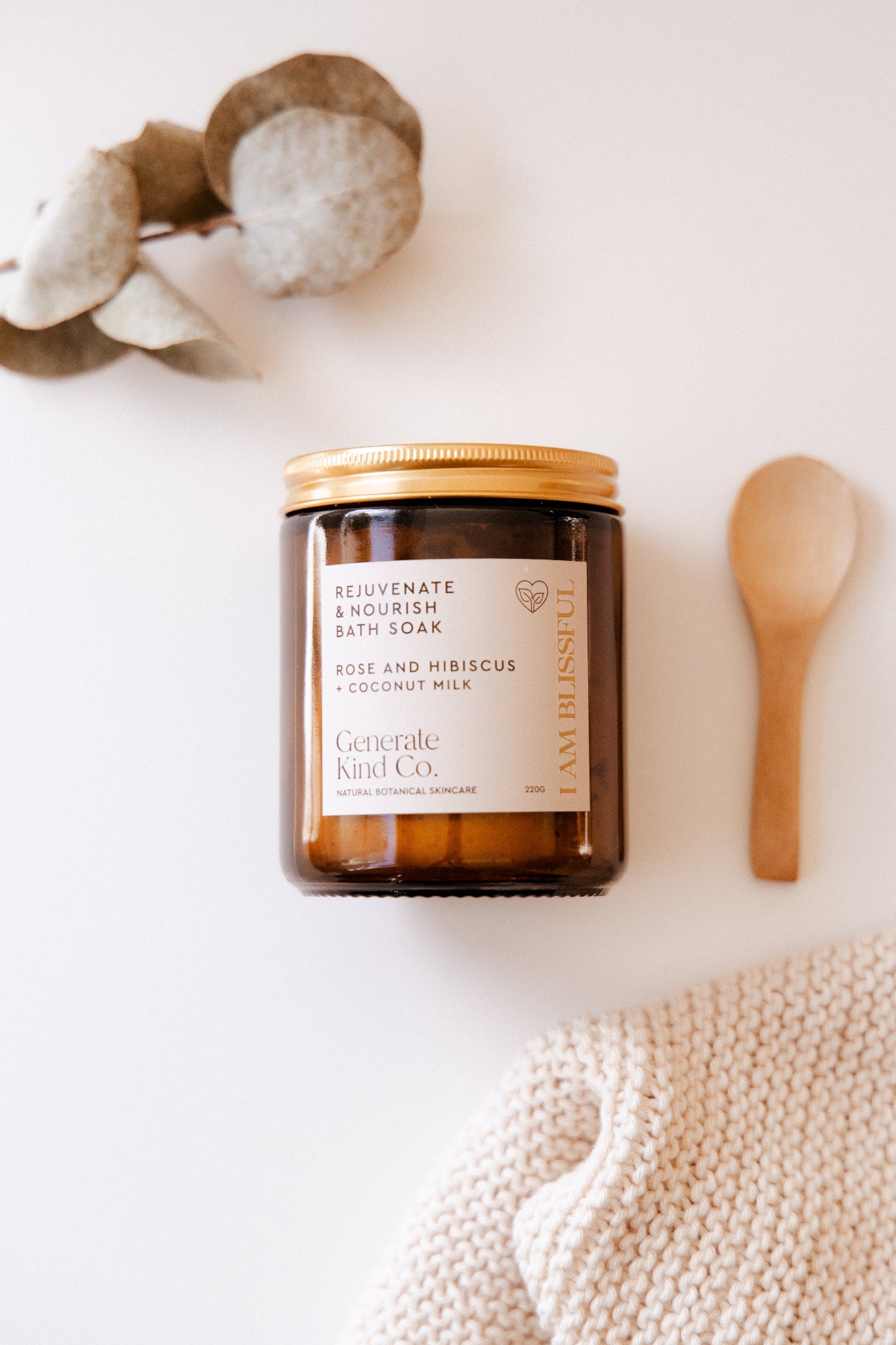 Jar of Generate Kind Co Bath Soak with a wooden spoon and textured fabric on a white background