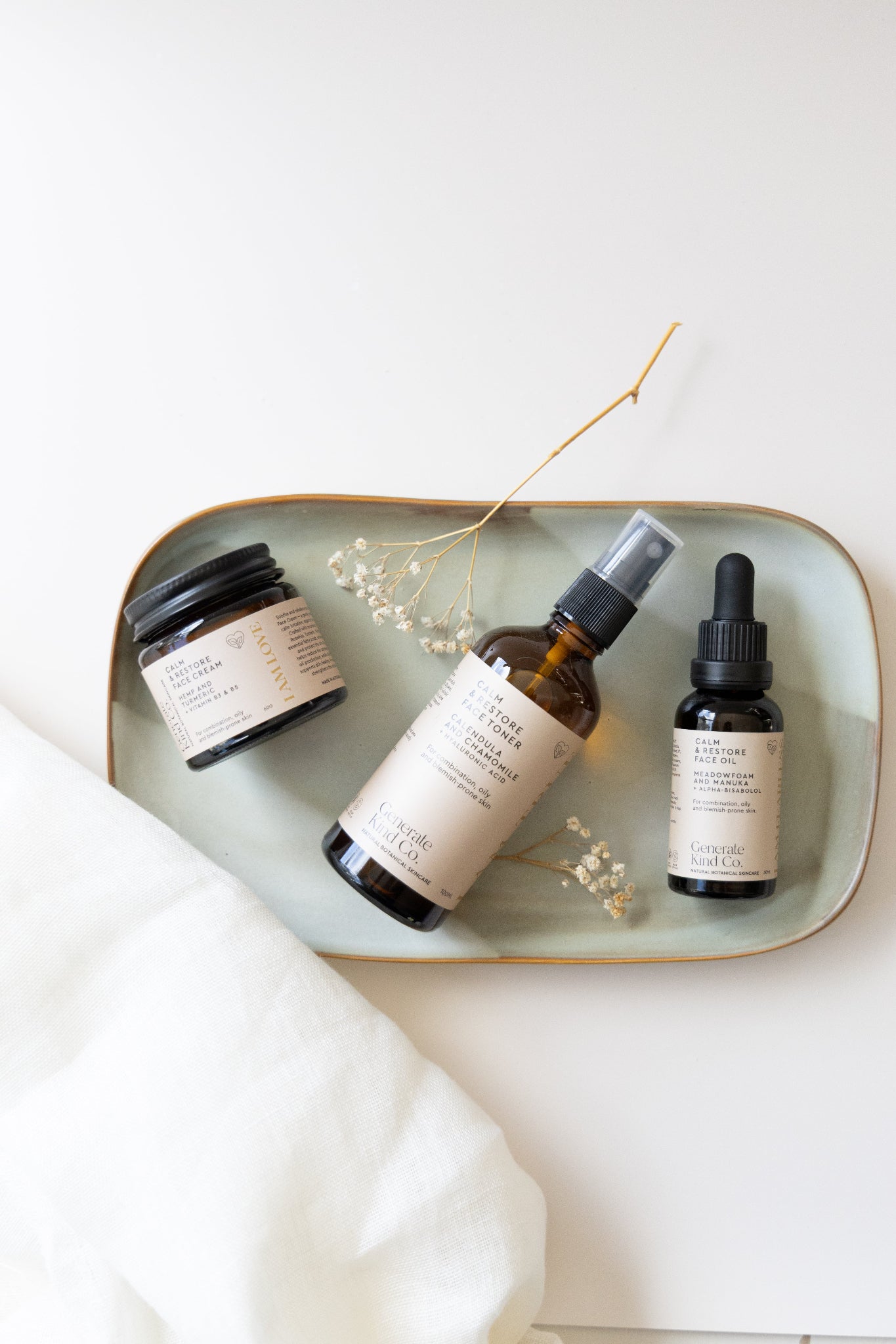 Generate KInd Co. Calm & Restore Skincare range laying on tray with dried botanicals and linen fabic