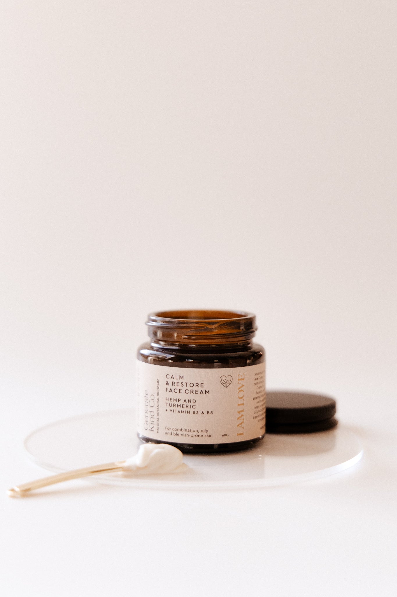 Jar of Calm & Restore face cream with a golden spatula showin cream texture on a white background