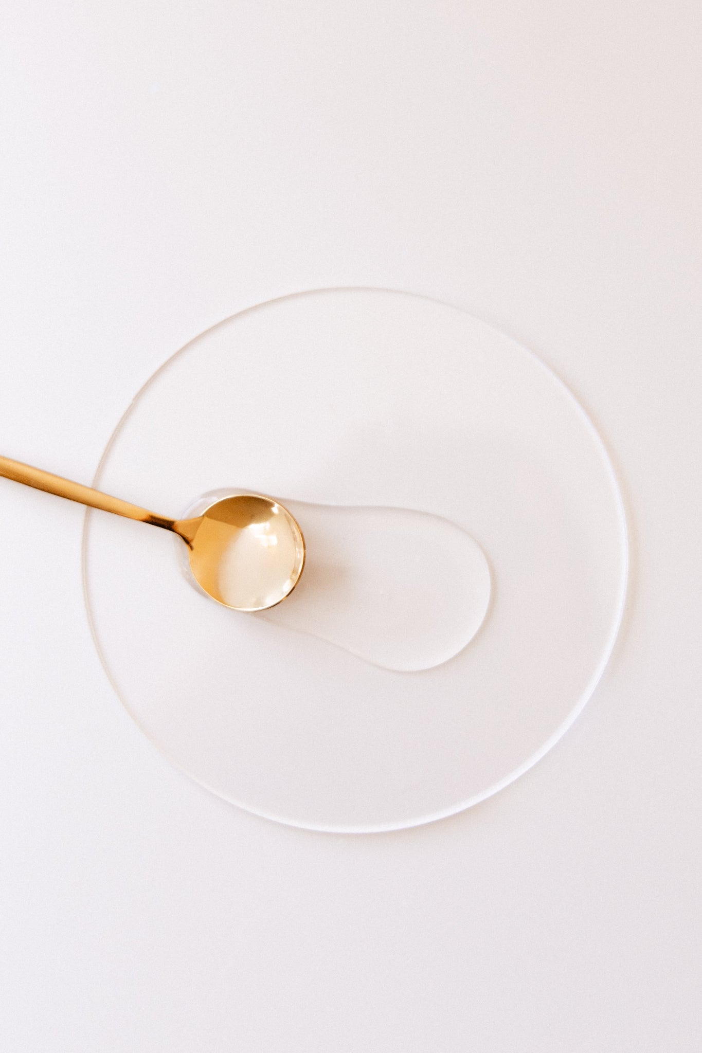 Gold spoon on a clear glass plate against a white background