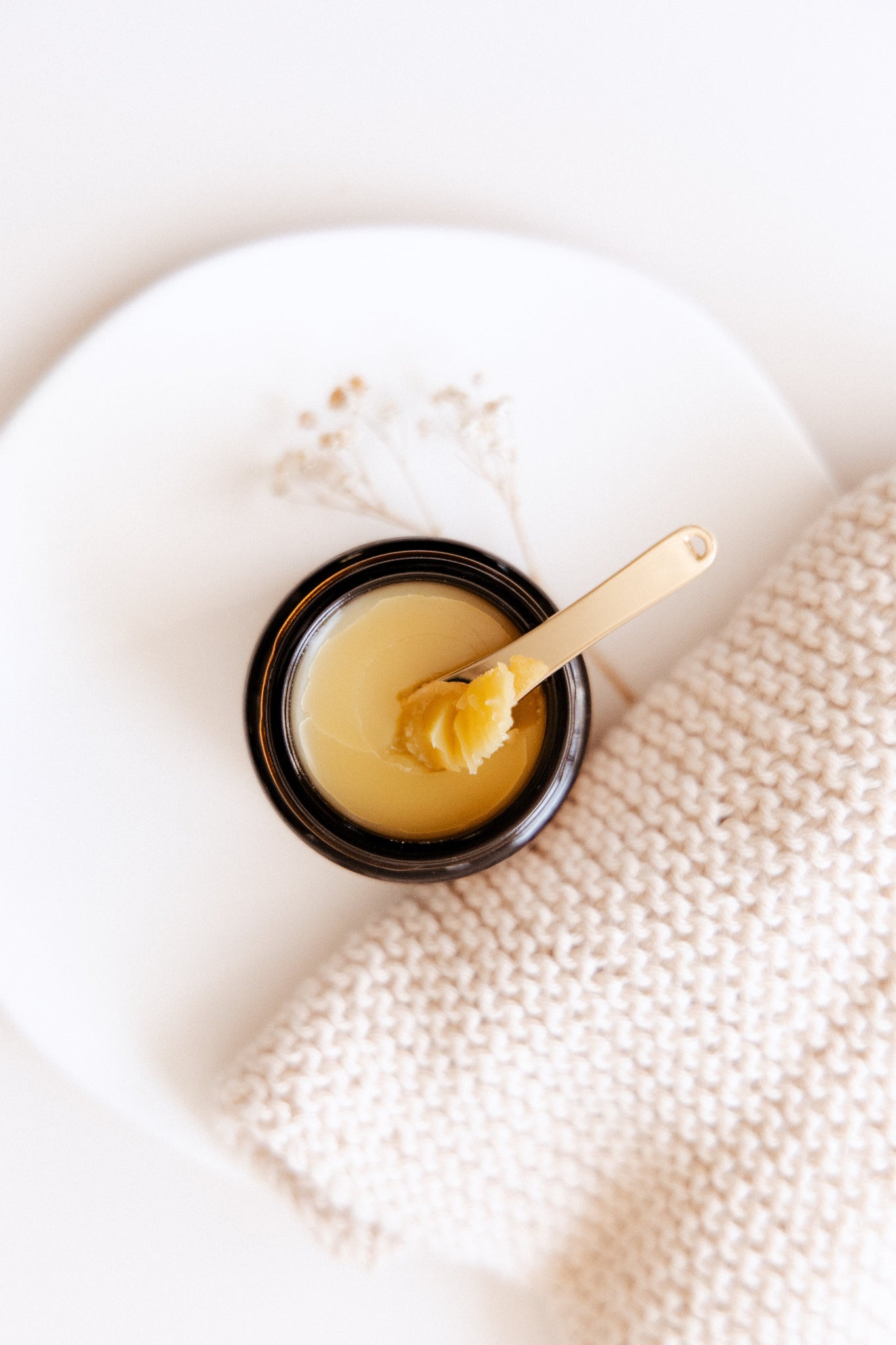 Kawakawa Balm Texture with a Golden applicator spoon on a textured white surface