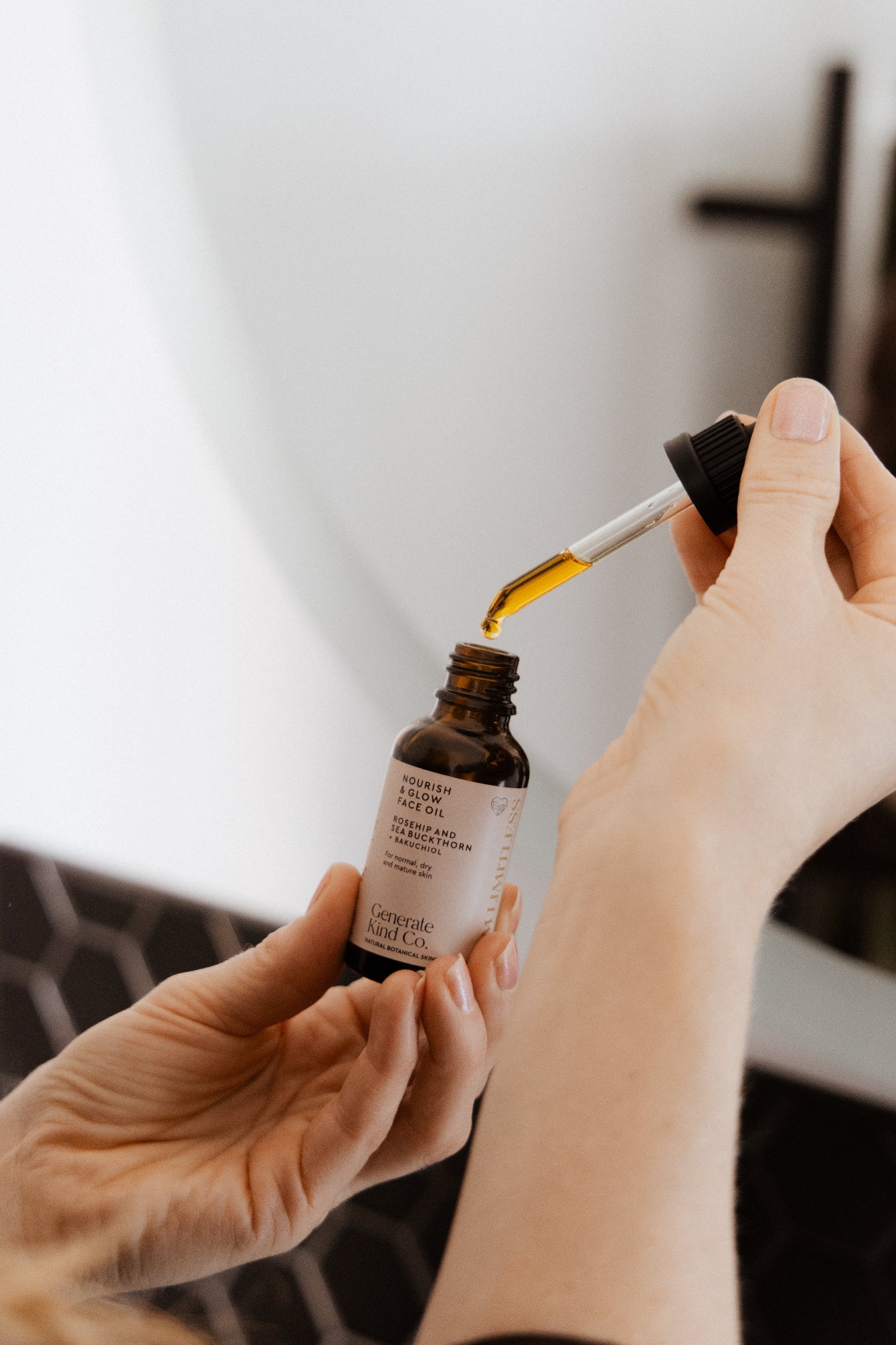 Person using a Nourish & Glow Face Oil dropperwith a blurred background