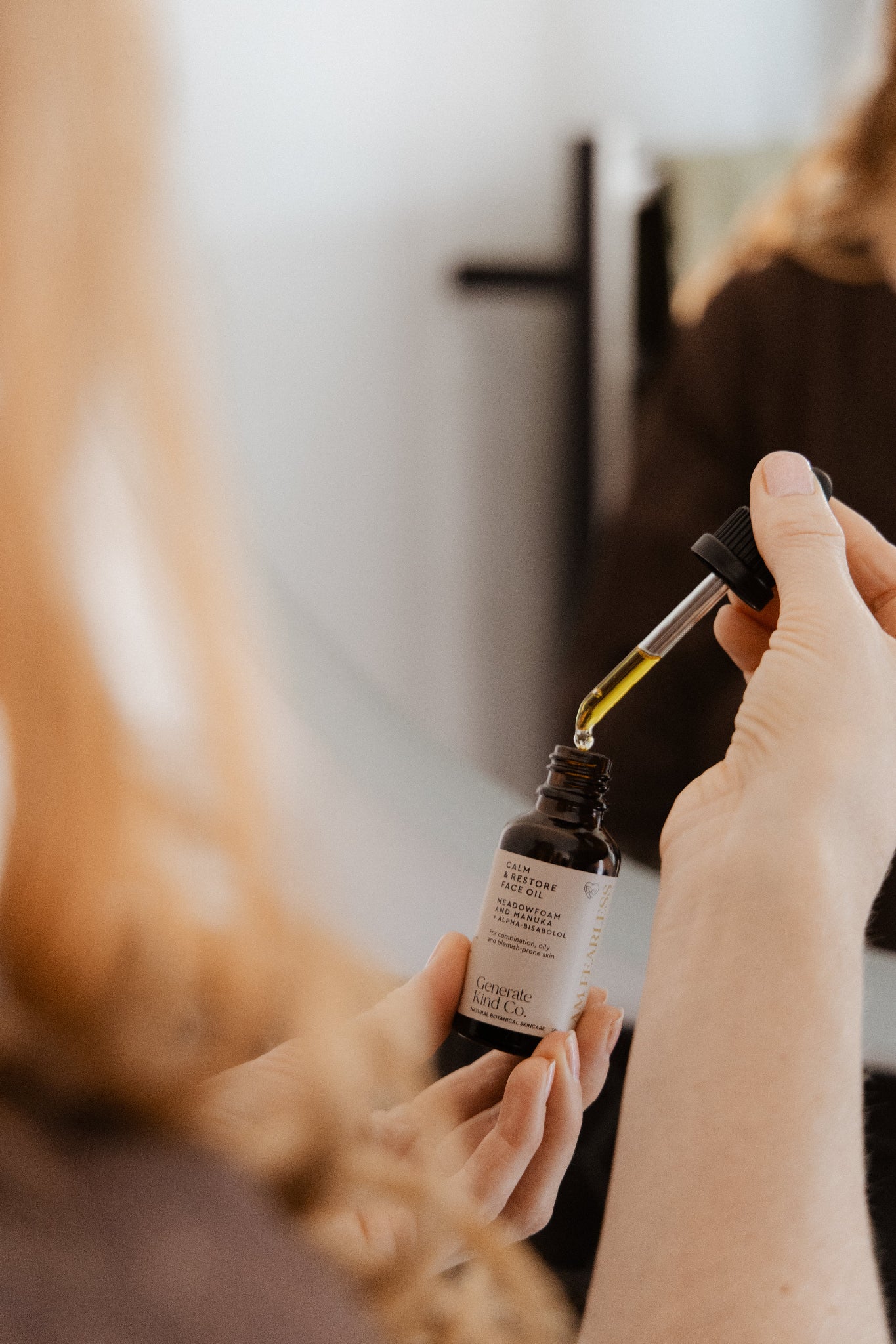 Person holding Caml & Restore Face oil dropper with a blurred background in bathroom