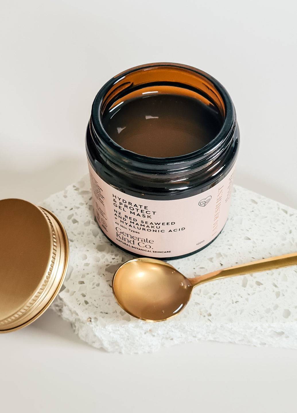 Cosmetic jar with a gold spoon on a textured surface