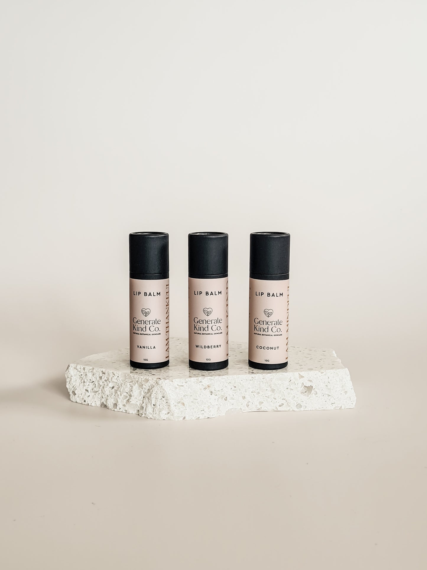Three lip balm containers on a textured white surface with a neutral background