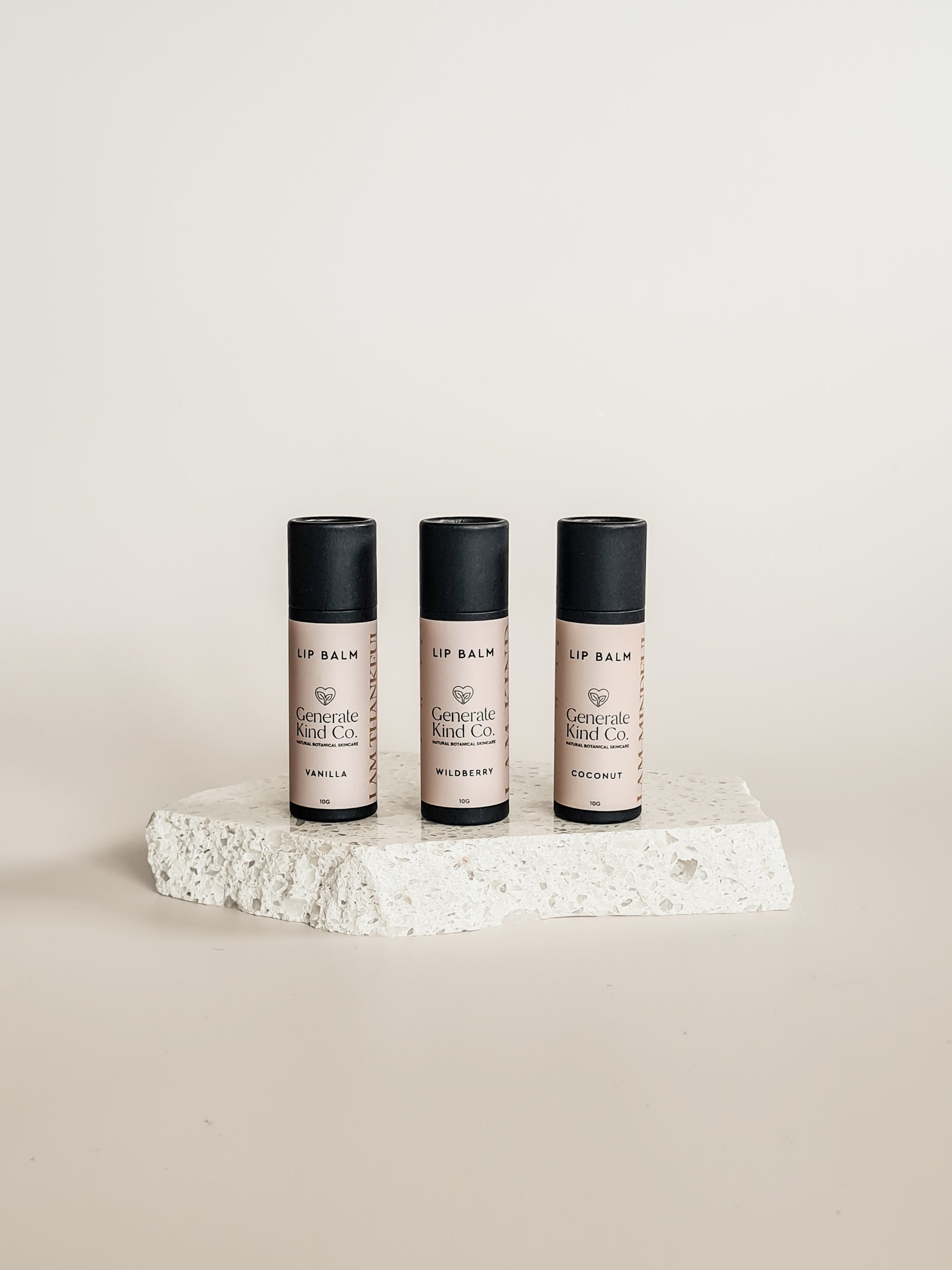 Three lip balm containers on a textured white surface with a neutral background