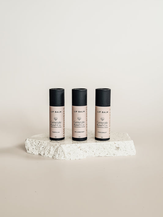 Three lip balm containers on a textured white surface with a neutral background